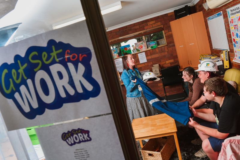 Two young men and a young woman sitting in a classroom with a Get Set for Work banner outside listen to an instructor at the Emerald Training Centre.